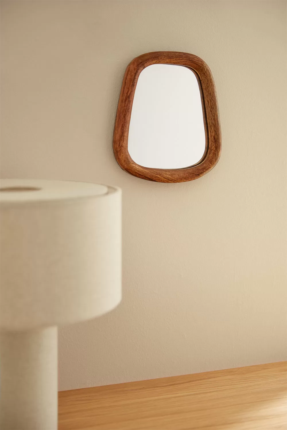 Espelho decorativo com moldura orgânica que amplifica a luz natural numa pequena sala de estar.